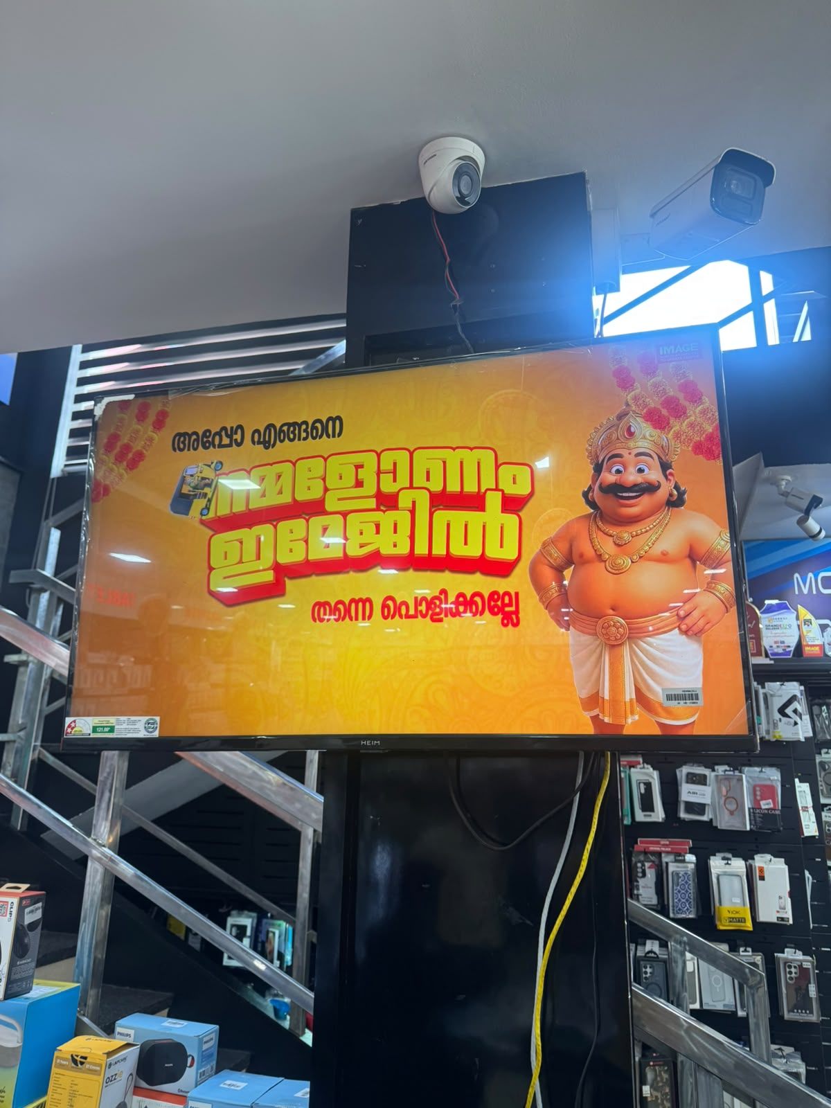 In-store digital TV screen showing IMAGE Mobiles & Computers' Onam campaign creative with the Maveli mascot